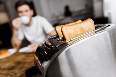 Genç adam ön plan üzerinde ekmek kızartma makinesi ile evde kahve içme