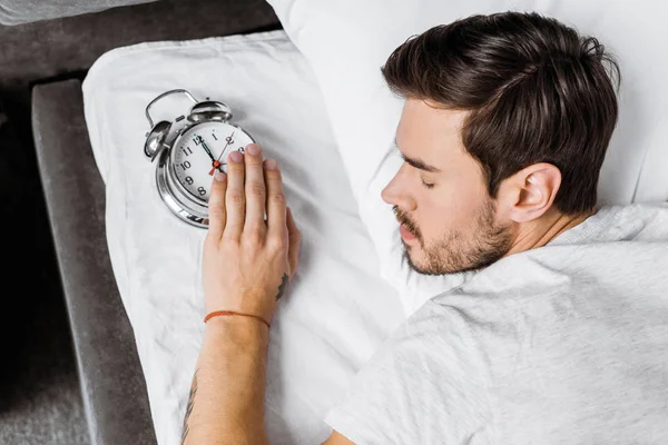 Vista Superior Del Joven Sosteniendo Despertador Durmiendo Cama — Foto de Stock