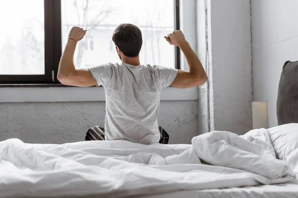ベッドに座ってストレッチ パジャマ姿で若い男の背面図 — ストック写真