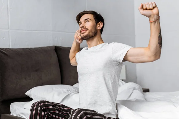 Schöner Bärtiger Junger Mann Schlafanzug Dehnt Sich Während Bett Sitzt — kostenloses Stockfoto