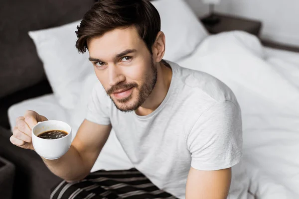 Jovem Bonito Segurando Xícara Café Sorrindo Para Câmera Enquanto Sentado — Fotografia de Stock