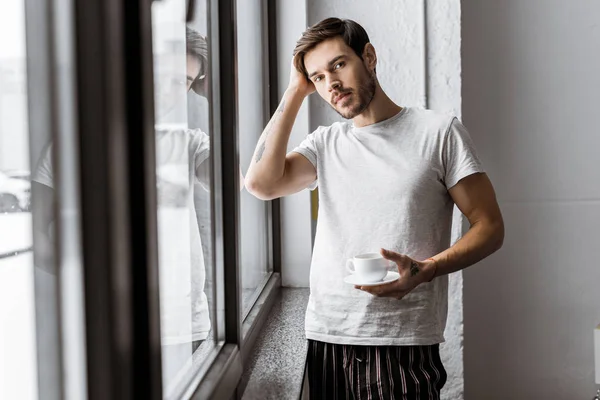 Joven Guapo Sosteniendo Una Taza Café Mirando Cámara Por Mañana — Foto de stock gratis