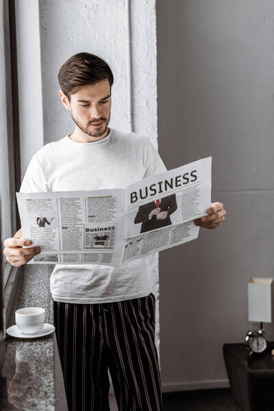 handsome young man in pajamas reading business newspaper at home  