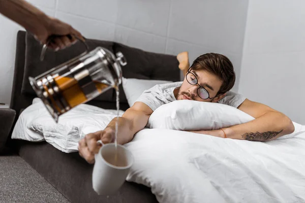 Vista Parcial Alguien Vertiendo Taza Mientras Hombre Somnoliento Anteojos Acostados — Foto de stock gratis