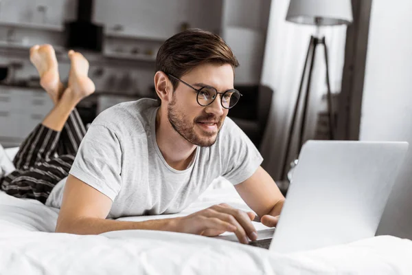 Smiling Young Man Eyeglasses Pajamas Using Laptop Bed — Stock Photo, Image