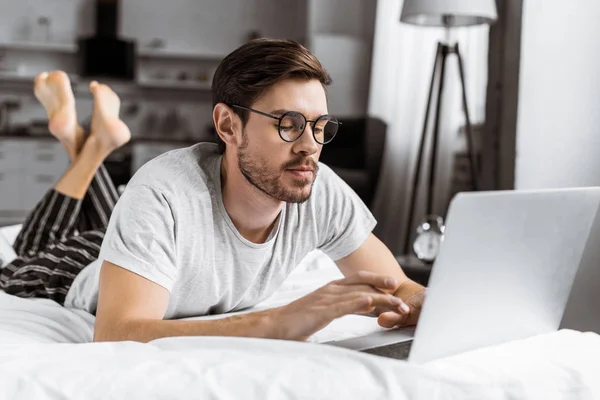 Όμορφος Νεαρός Άνδρας Γυαλιά Και Πιτζάμες Χρησιμοποιώντας Laptop Στο Κρεβάτι — Δωρεάν Φωτογραφία