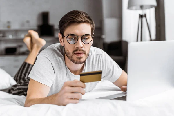 Young Man Eyeglasses Pajamas Holding Credit Card Using Laptop Bed — Free Stock Photo