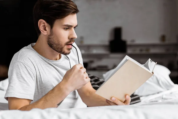 Jovem Segurando Óculos Lendo Livro Enquanto Deitado Cama — Fotografia de Stock Grátis