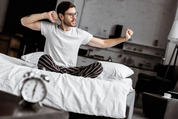 Joven Guapo Pijama Anteojos Estirándose Mientras Está Sentado Cama Por — Foto de stock gratuita