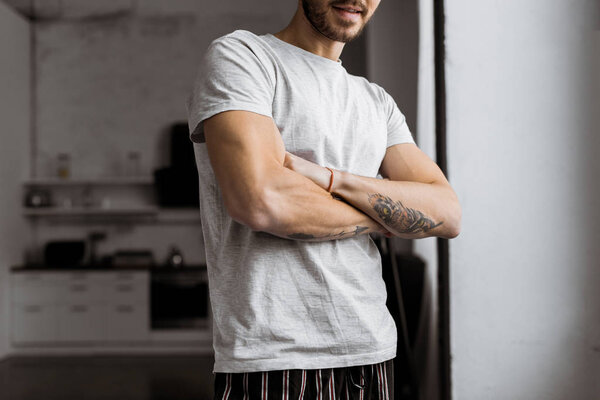 cropped shot of handsome young man with crossed arms in pajamas standing at home