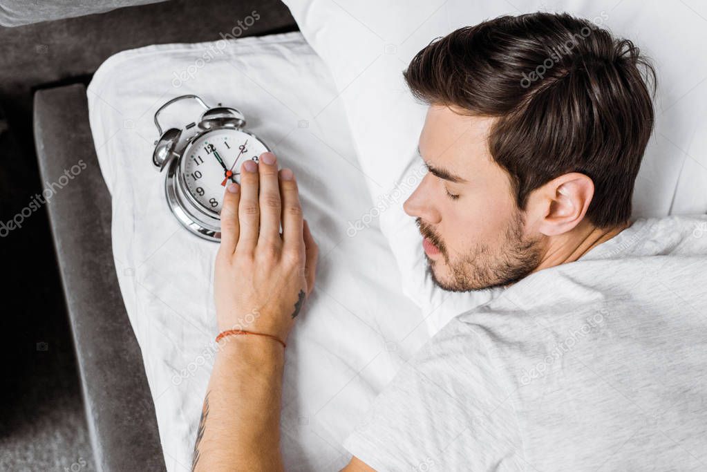 top view of young man holding alarm clock and sleeping in bed