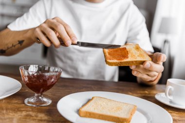 cropped shot of man applying jam onto toast at home clipart