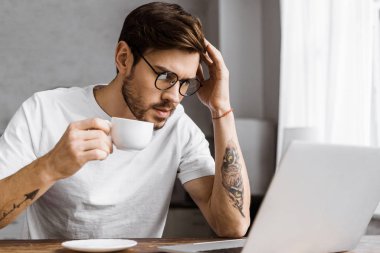 evde dizüstü bilgisayar ekranına bakarak kahve ile genç freelancer vurguladı