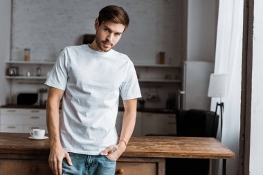 mutfak masasında yaslanmış ve evde kameraya bakarak çekici bir genç adam