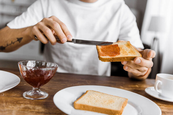 cropped shot of man applying jam onto toast at home