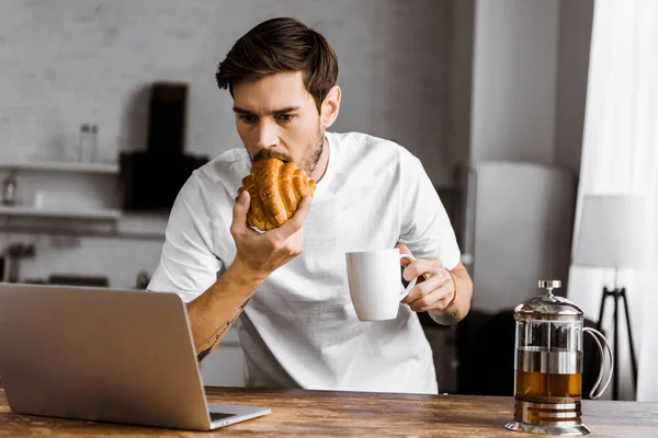Tânăr Freelancer Emoțional Ceașcă Ceai Croissant Laptop Care Lucrează Bucătărie — Fotografie de stoc gratuită