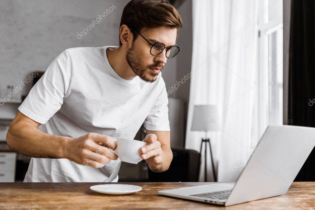 attractive young freelancer with coffee working with laptop at home