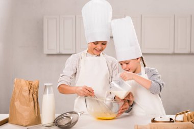 kid pouring milk into bowl while brother whisking at table in kitchen  clipart