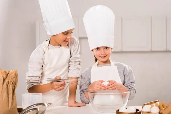 little children in aprons and chef hats preparing at table in kitchen
