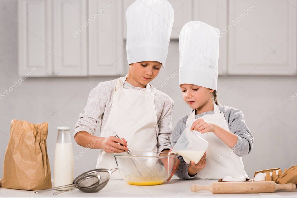 kid pouring milk into bowl while brother whisking at table in kitchen 