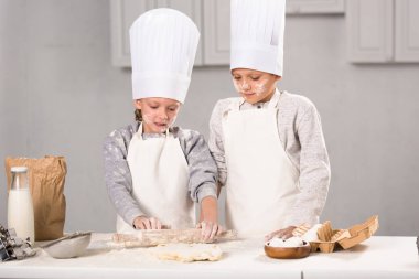 kız ve erkek kardeş önlük ve chef şapka hamuru oklava ile mutfak masasında yapma