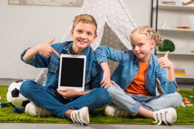 gülümseyen çocuk dijital tablet ile boş bir ekran ve kız kardeşi çevre çadır evde yukarı gösteren işaret