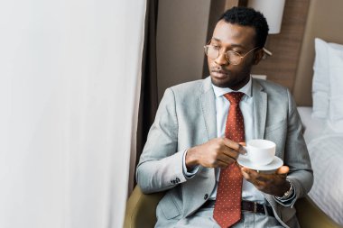 serious african american businessman holding cup of coffee and looking at window