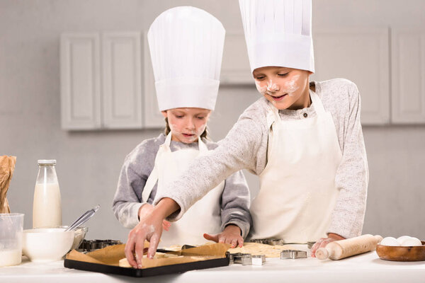 adorable sister and her brother putting dough for cookies on baking tray in kitchen