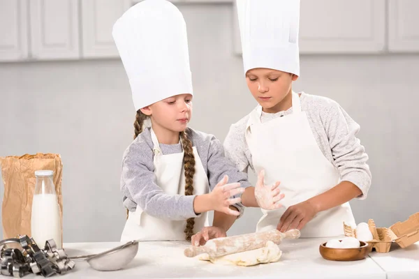 エプロンやキッチンのテーブルで麺棒で生地を作るシェフ帽子子供  — 無料ストックフォト