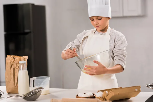 Focused Boy Chef Hat Apron Whisking Eggs Bowl Table Kitchen — Stock Photo, Image