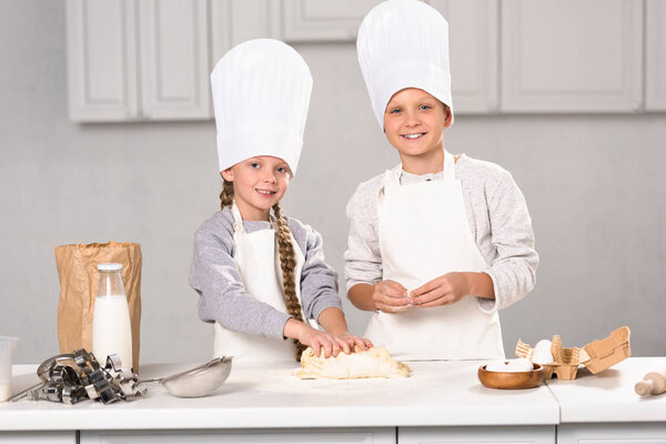 cheerful brother and sister preparing dough for cookies at table in kitchen