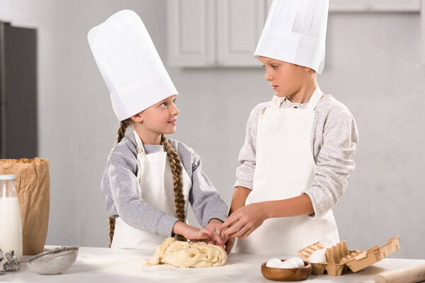 brother and sister preparing dough for cookies at table in kitchen