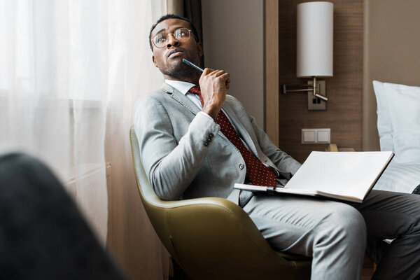 thoughtful african american businessman with diary sitting in hotel room