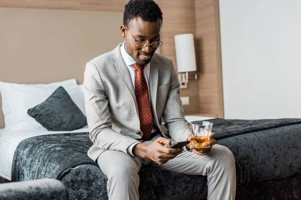 Sonriente Hombre Negocios Afroamericano Con Vaso Coñac Usando Teléfono Inteligente —  Fotos de Stock