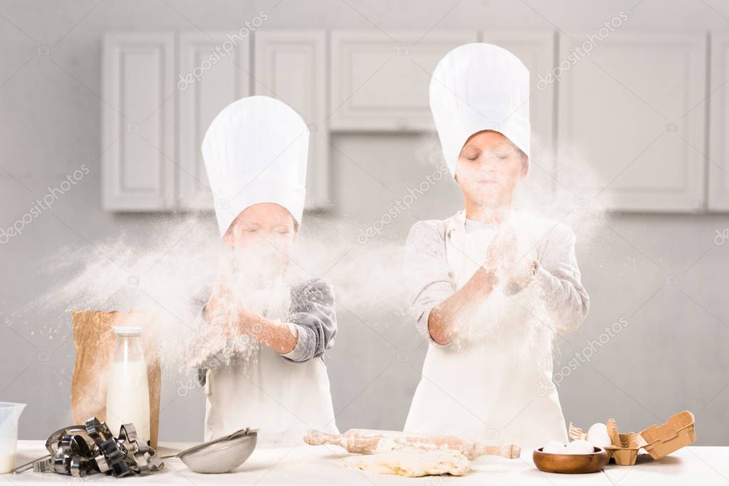 selective focus of brother and sister in chef hats having fun with flour in kitchen 