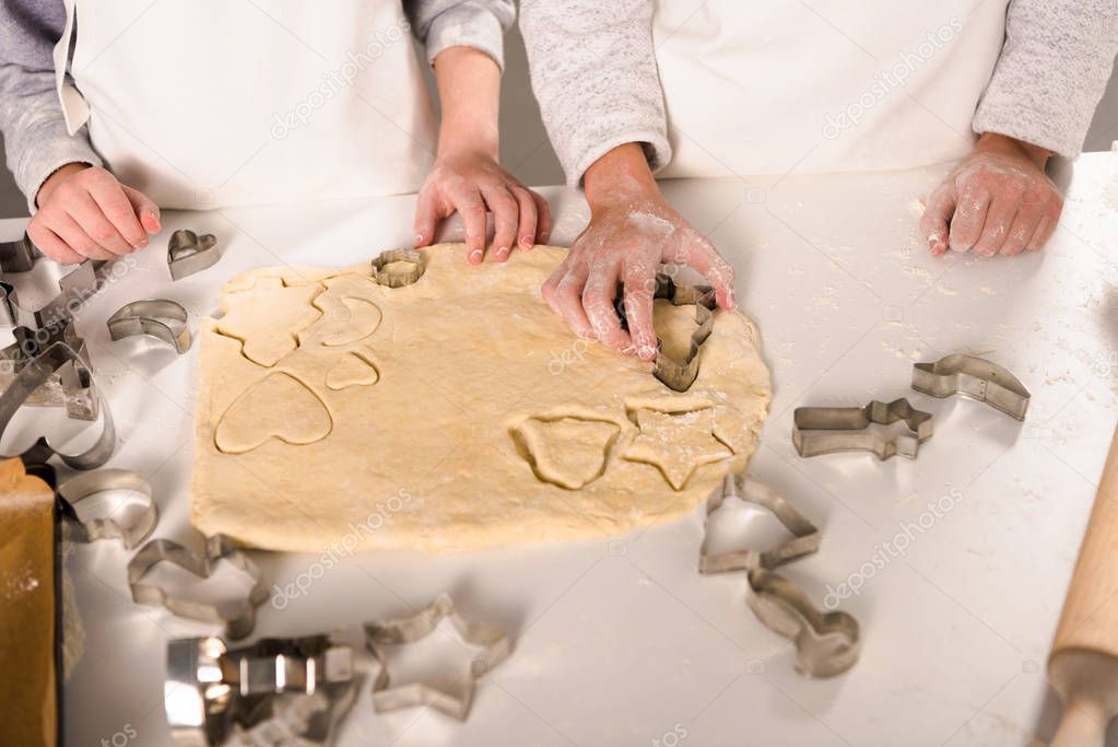 cropped image of kids in aprons cutting out dough for cookies at table in kitchen