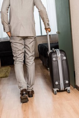 arkadan işadamı gri elbiseli görünüşü ile otel odasına geliyor seyahat çantası