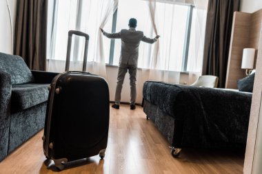 Otel odasındaki bavulun seçici odak noktası iş adamlarının pencere perdelerini açması.