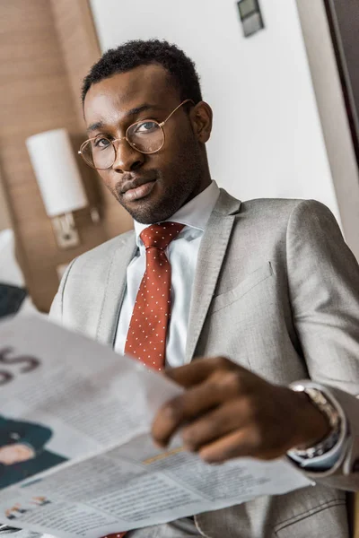 新聞を押しながらカメラ目線のスーツでアフリカ系アメリカ人のビジネスマン — ストック写真