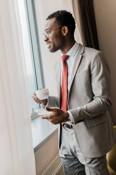 一杯のコーヒーを保持していると ウィンドウを見てハンサムなアフリカ系アメリカ人のビジネスマン — ストック写真