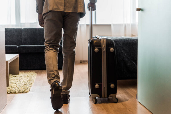 cropped view of businessman in suit with baggage coming into hotel room