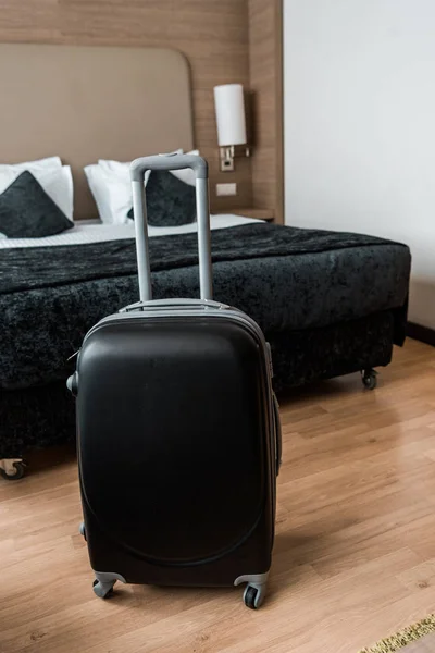 black travel bag in hotel room with bed