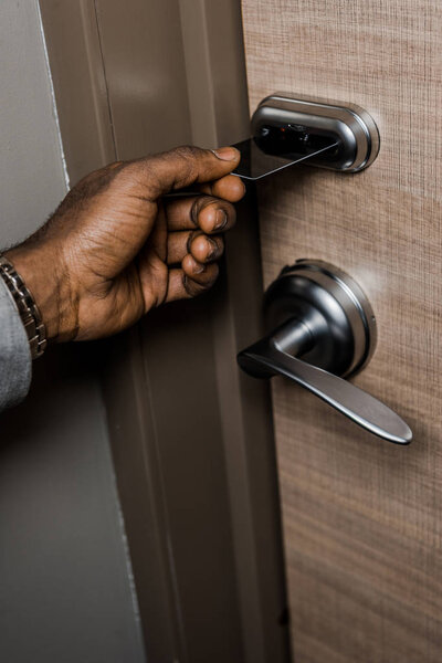 cropped view of african american man opening door with electronic key card in hotel