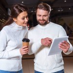 Portrait of couple in white knitted sweaters using digital tablet together