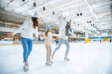 Aile tutuşup birlikte buz pistinde paten yaparken gülümseyen