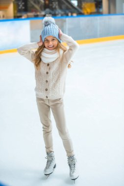 smiling adorable kid in sweater and hat on skating rink clipart