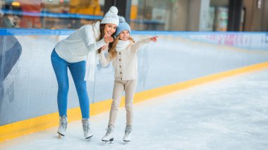 Anne ve kızı uzağa işaret buz pateni pisti üzerinde gülümseyen