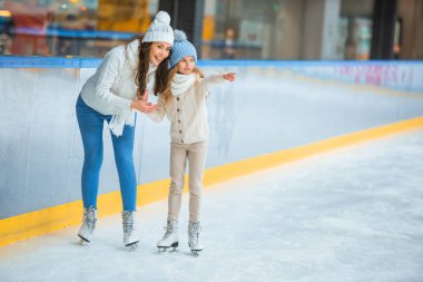 smiling daughter showing something to mother on skating rink clipart