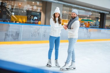 çift örgü şapka ve kazak buz pateni pisti üzerinde gülümseyen