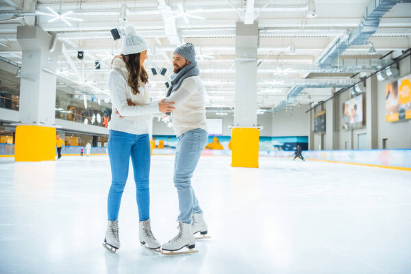 couple in knitted sweaters and hats skating together on ice rink